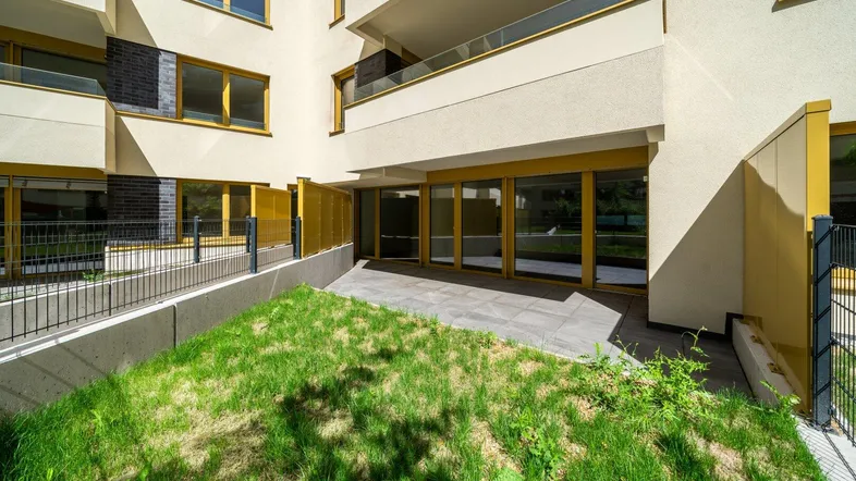 Erdgeschoss-Terrasse mit Fliesenboden und angrenzender Rasenfläche vor einem modernen Gebäude.