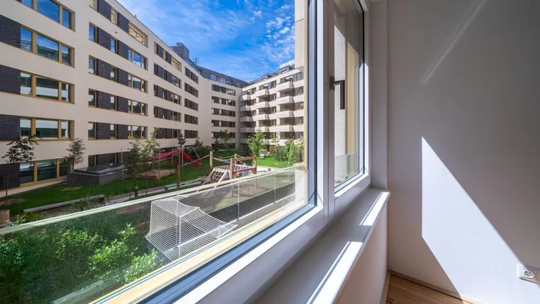 Blick aus dem Fenster in einen modernen Innenhof mit Spielplatz und umliegenden Wohngebäuden.