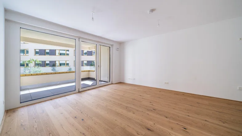 Helles Zimmer mit Parkettboden und Zugang zu einem geräumigen Balkon, ideal für Wohn- oder Schlafbereich.
