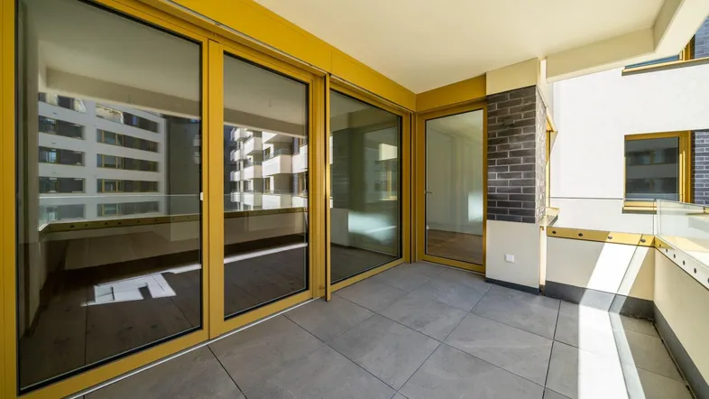 Geräumiger Balkon mit modernen Fliesen, gelben Fensterrahmen und Blick auf die umliegenden Gebäude.