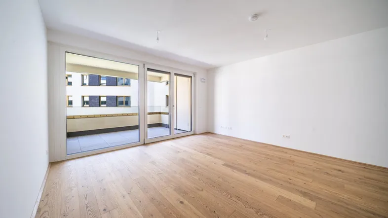 Heller, leerer Wohnraum mit Holzboden und Zugang zu einem Balkon, ideal für individuelle Gestaltung.