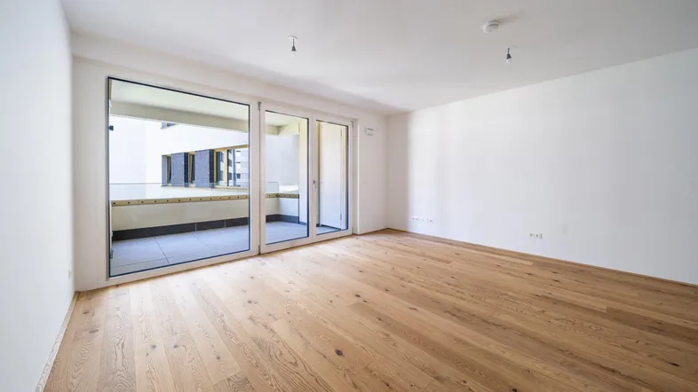 Heller Wohnraum mit Echtholzparkett und großen Schiebetüren zum Balkon, ideal für offenes Wohnen.