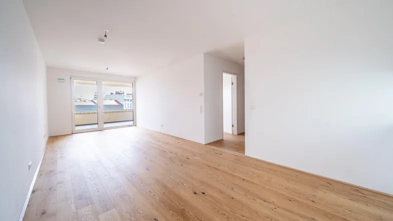 Helles, leeres Zimmer mit Holzboden und Zugang zu einem Balkon, bereit zum Einzug.
