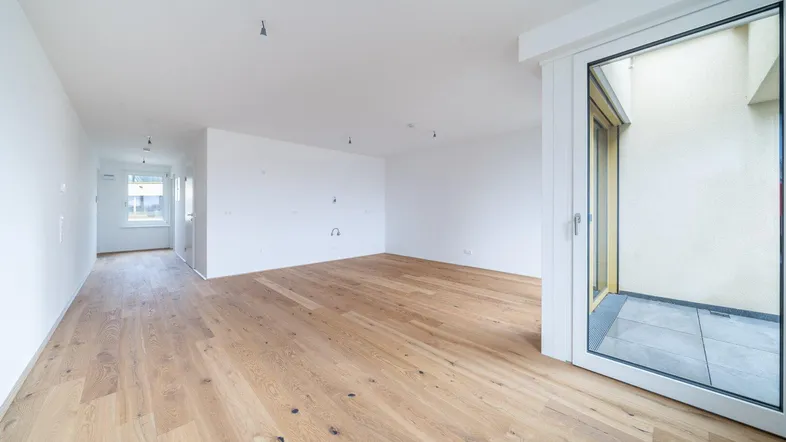 Heller, leerer Raum mit Holzboden und Zugang zu einem kleinen Außenbereich.