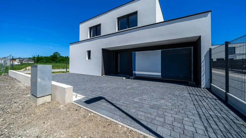 Moderne Neubau-Doppelhaushälfte mit gepflasterter Einfahrt und klaren Linien unter blauem Himmel.