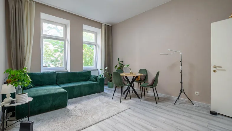 Helles Wohnzimmer mit grünem Sofa, kleinem Esstisch und hellem Laminatboden.