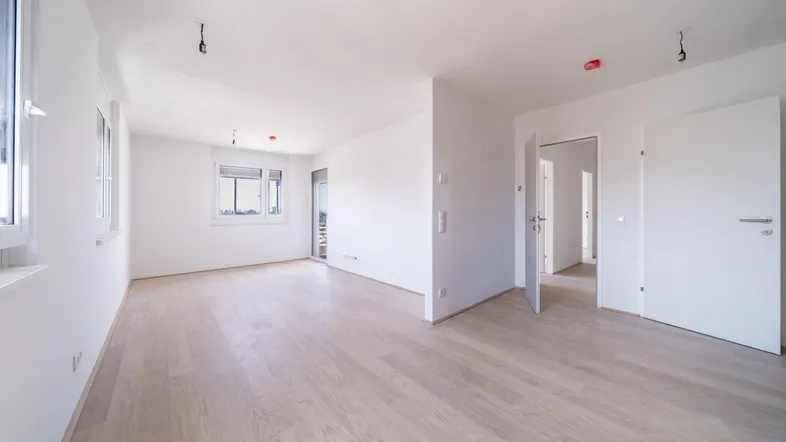 Helles, leeres Wohnzimmer mit hellem Parkettboden und weißen Wänden, bereit zur Einrichtung.