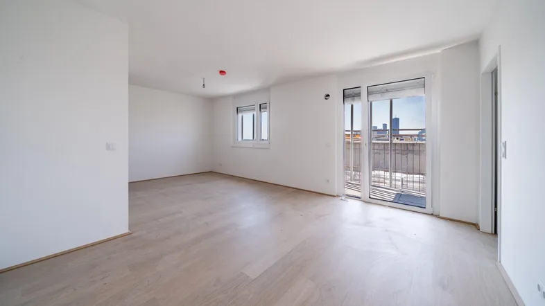 Heller, leerer Wohnbereich mit modernem Holzboden und Zugang zu einem Balkon.