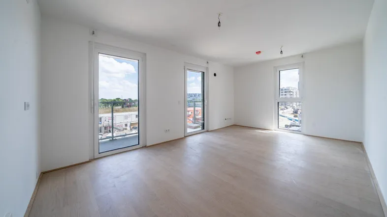 Helles Zimmer mit Holzboden und Zugang zu mehreren Fenstern, Blick auf eine Baustelle.
