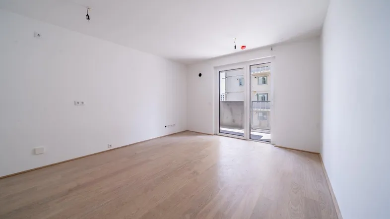 Helles Zimmer mit Holzboden und Zugang zu einem Balkon, ideal als Wohn- oder Schlafbereich.