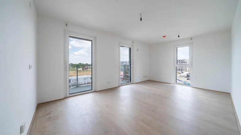 Helles, leeres Wohnzimmer mit großen Fenstern und hellem Laminatboden, bereit zur Einrichtung.