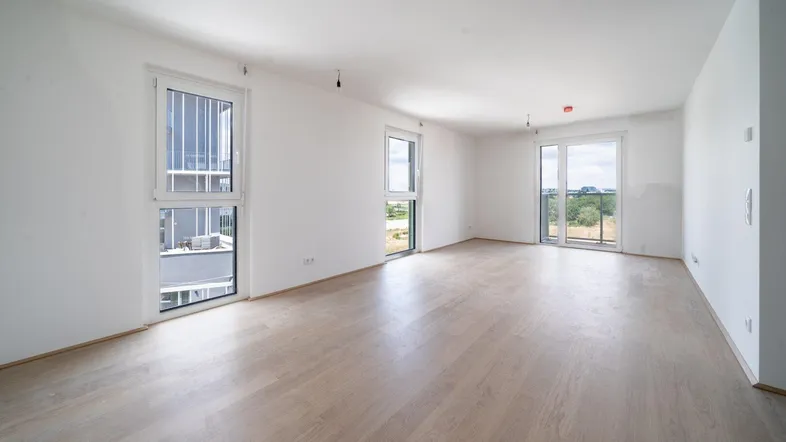 Helles, unmöbliertes Wohnzimmer mit Laminatboden und Zugang zu mehreren Balkonen.