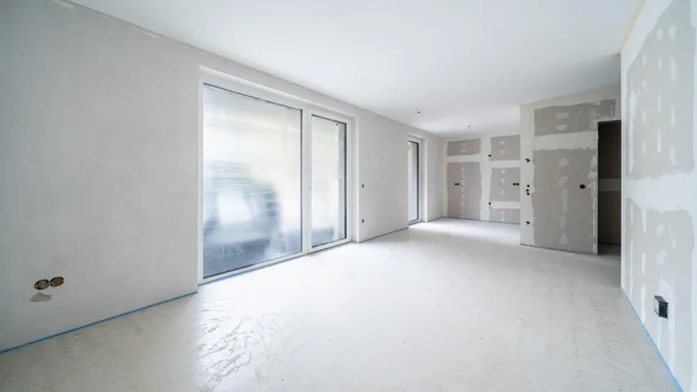 Heller Innenraum im Rohbau mit großen Schiebetüren und vorbereiteten Wänden für den Ausbau.