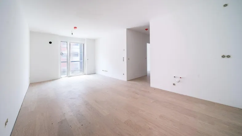 Geräumiges, helles Wohnzimmer mit Holzboden und Zugang zu einem Balkon in einem Neubau.