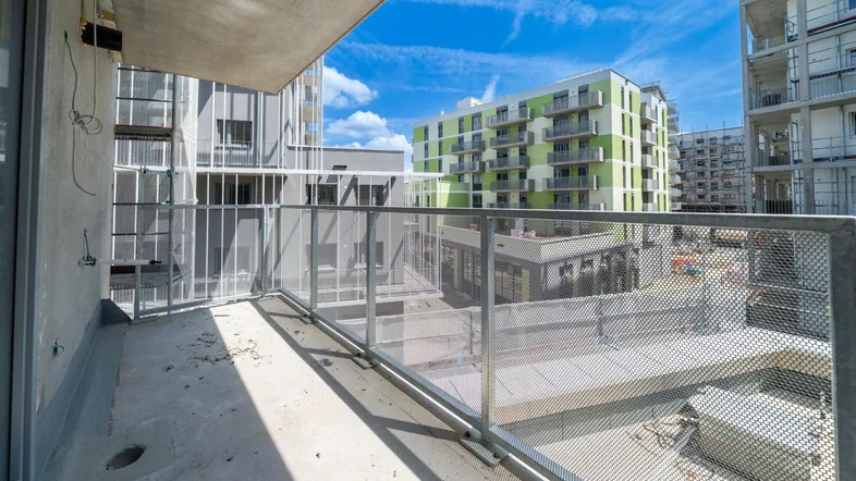 Unfertiger Balkon mit Metallgeländer und Blick auf umliegende Neubauten und Baustelle.