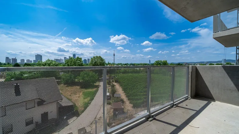 Geräumiger Balkon mit Metallgeländer und weitem Blick über die Stadt und grüne Umgebung.