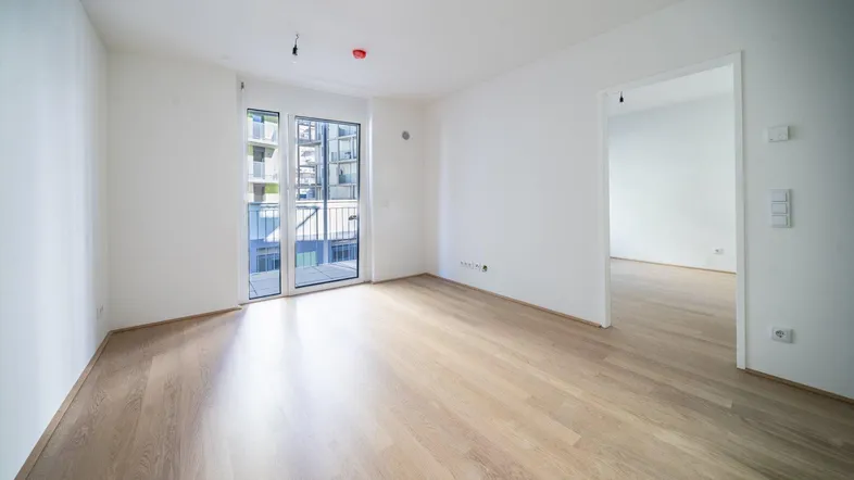 Helles Zimmer mit Parkettboden und Zugang zu einem Balkon, bereit zum Einzug.