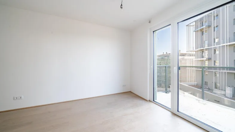 Helles, unmöbliertes Zimmer mit Parkettboden und großen Fenstern, die viel Tageslicht hereinlassen.
