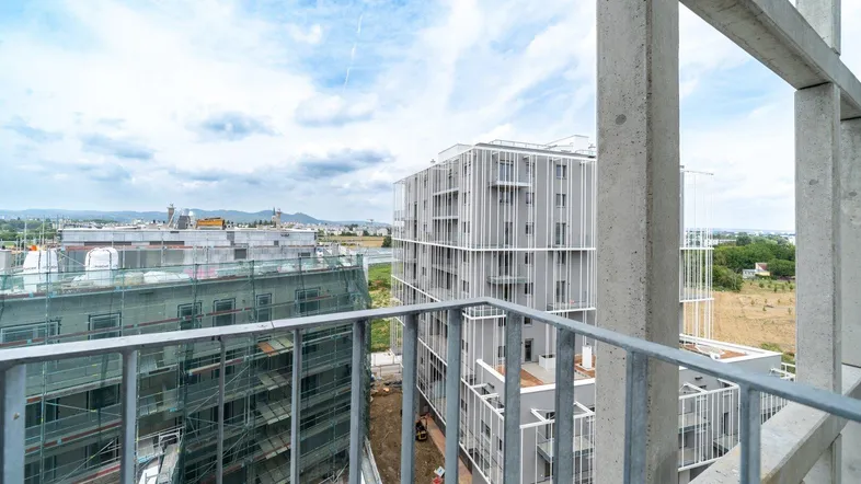 Blick von einem Balkon auf moderne Gebäude und die umliegende Stadtlandschaft unter bewölktem Himmel.