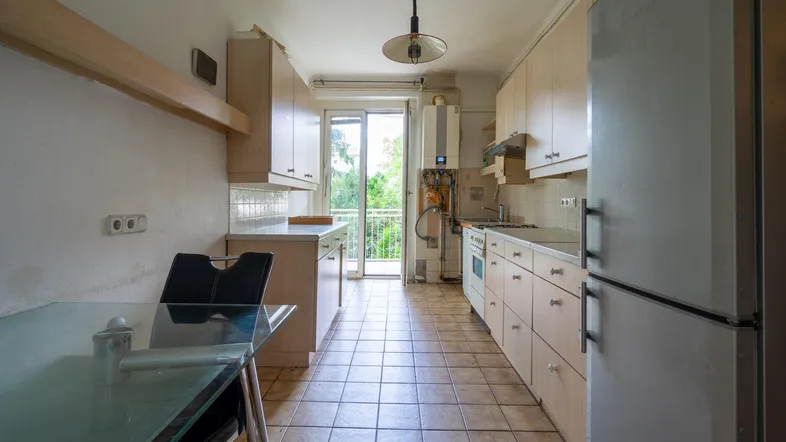Helle Küche mit Fliesenboden, Einbauschränken und Zugang zu einem kleinen Balkon.
