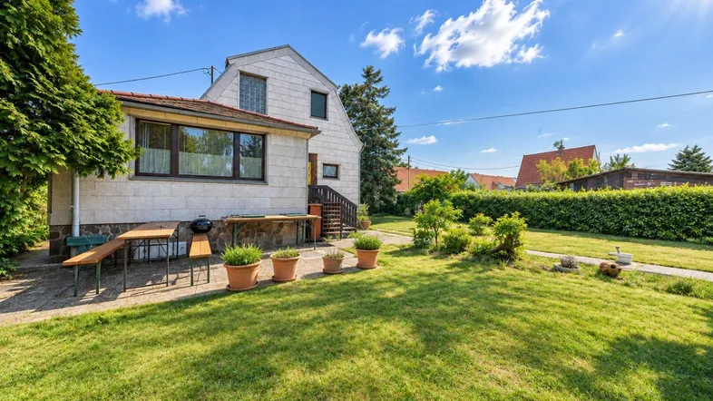 Gepflegter Gartenbereich mit Rasenfläche, Sträuchern und einem kleinen Sitzbereich neben dem Haus.