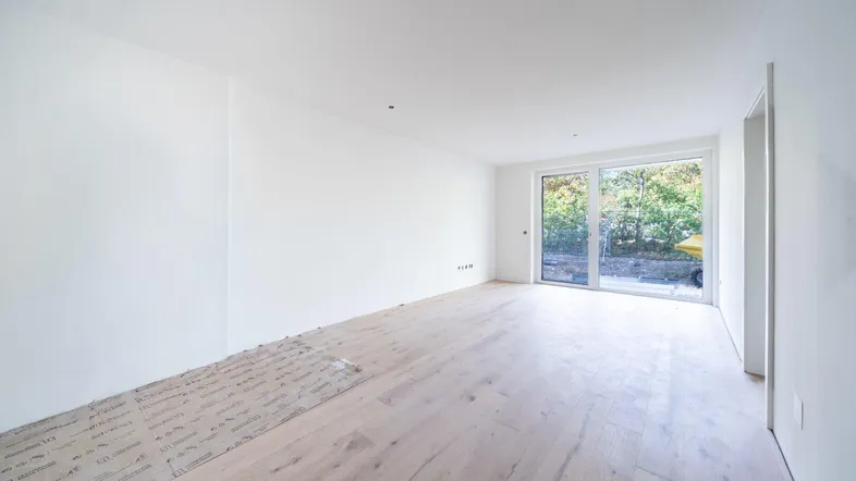 Heller, unmöblierter Raum mit großen Fenstern und Holzboden, bereit für den Innenausbau.
