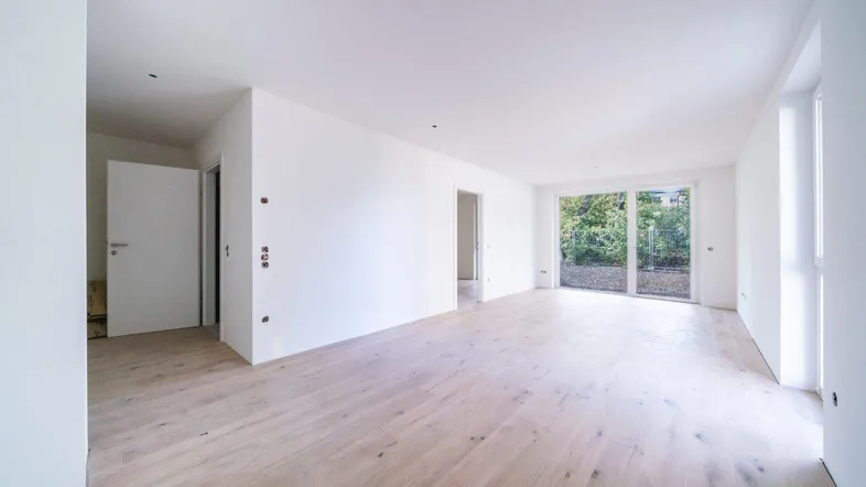 Helles, leeres Zimmer mit Holzboden und Zugang zu einer Terrasse oder Garten.
