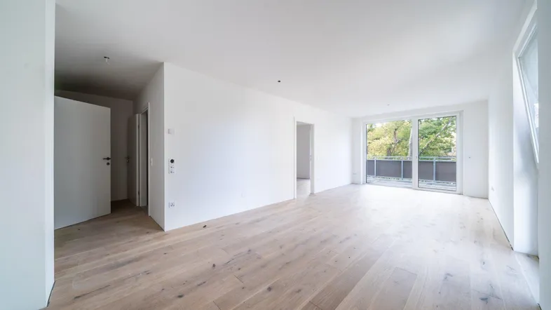 Helles und geräumiges Wohnzimmer mit neuem Holzboden und Zugang zum Balkon.
