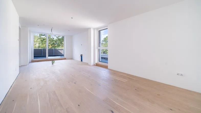 Helles, leeres Wohnzimmer mit neuem Holzboden und großen Fenstern, die Zugang zu einem Balkon bieten.