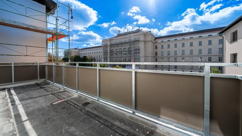 Sonnige Terrasse im Bau mit Blick auf ein großes Gebäude und Gerüst im Hintergrund.