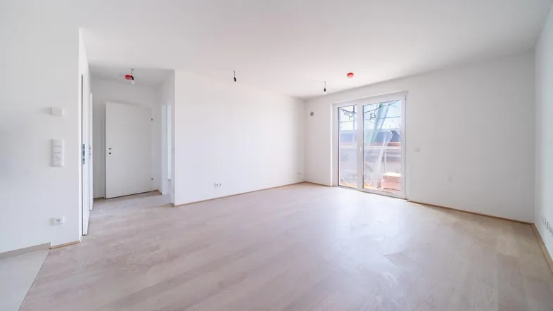 Helles, leeres Wohnzimmer mit neuem Parkettboden und Zugang zu einem zukünftigen Außenbereich.