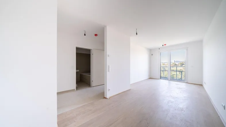 Heller, leerer Wohnbereich mit hellem Holzfußboden und Zugang zu einem Balkon.
