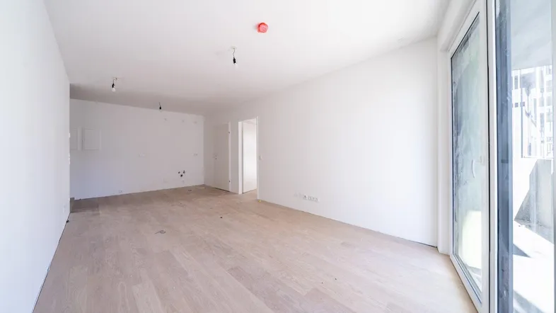 Helles, leeres Zimmer mit Parkettboden und Zugang zu einem Balkon, bereit für die individuelle Gestaltung.