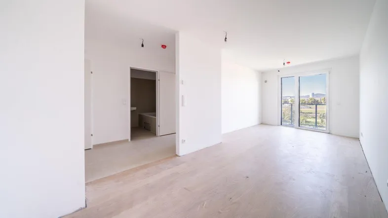 Helles, unmöbliertes Wohnzimmer mit Parkettboden und Zugang zu einem Balkon in einem Neubau.