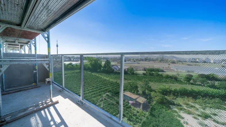Blick von einem im Bau befindlichen Balkon mit Gerüst auf grüne Felder und die Stadt.
