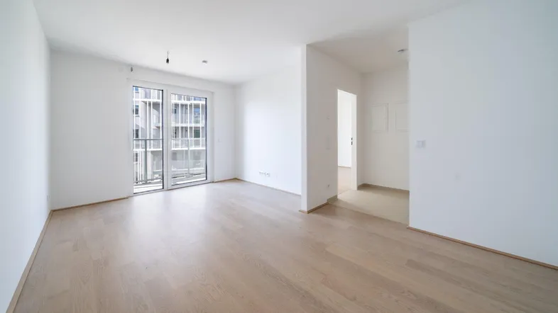 Helles, leeres Zimmer mit Holzboden und Zugang zu einem Balkon, bereit zur individuellen Gestaltung.