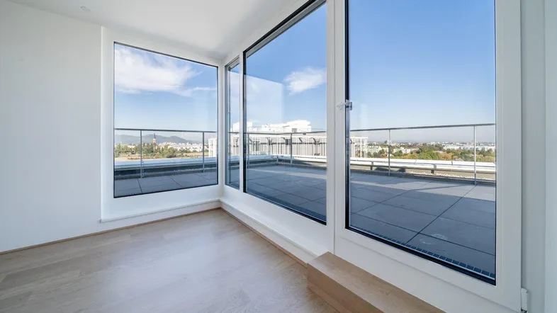 Heller Raum mit großen Fenstern und Zugang zu einer Dachterrasse mit Weitblick.