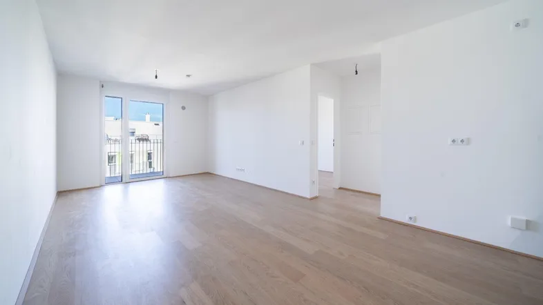 Helles, leeres Wohnzimmer mit Parkettboden und Zugang zu einem französischen Balkon.