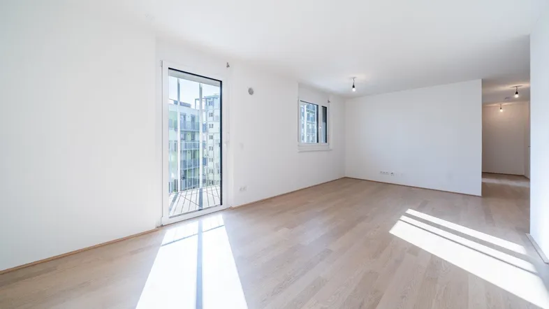 Helles, leeres Wohnzimmer mit Parkettboden und Zugang zu einem Balkon, ideal für neue Einrichtung.