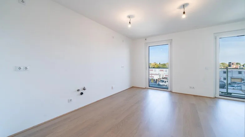 Heller, leerer Wohnküchenbereich mit Parkettboden und Zugang zu einem Balkon, bereit zur Gestaltung.