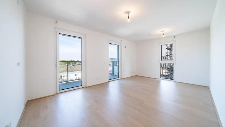 Helles, leeres Zimmer mit Parkettboden und Zugang zu mehreren Balkonen, ideal für Wohn- oder Schlafbereich.