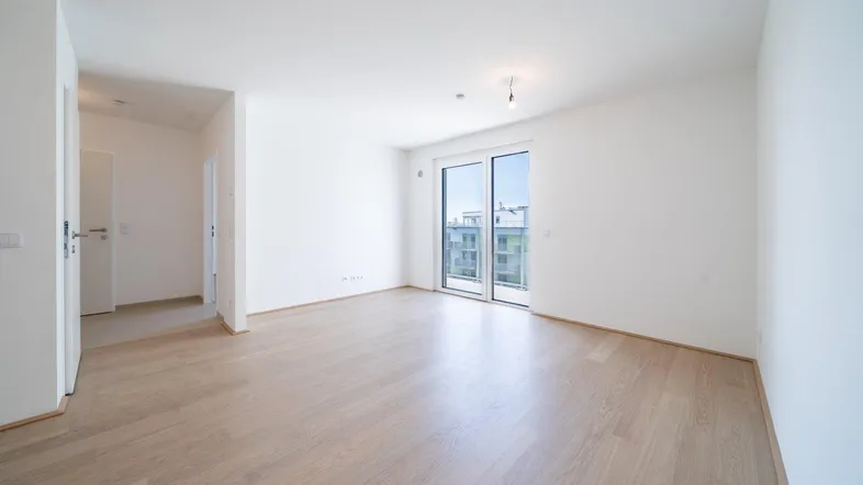 Helles, unmöbliertes Wohnzimmer mit Parkettboden und großen Schiebetüren zum Balkon.