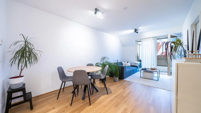 Heller Wohn- und Essbereich mit Holzboden, modernem Sofa und Zugang zum Balkon.