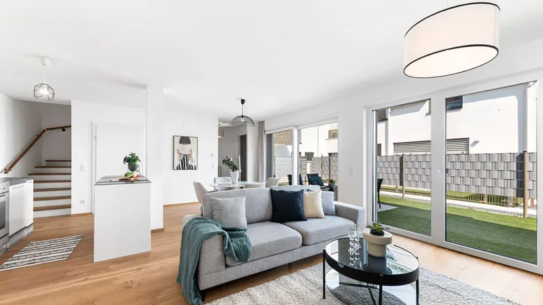 Helles, offenes Wohn- und Esszimmer mit Holzboden, bequemer Couch und Zugang zur Terrasse.