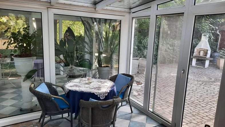 Heller Wintergarten mit Essbereich und Blick in den Garten mit Grillplatz.