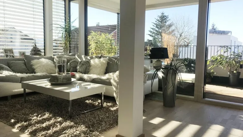Helles Wohnzimmer mit großen Fensterfronten, Holzboden und Zugang zur Terrasse.