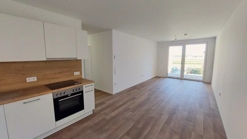 Heller, offener Wohn- und Essbereich mit integrierter Küche und Zugang zu einem Balkon.