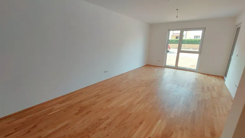 Heller Wohnraum mit neuem Parkettboden und Zugang zu einer Außenterrasse.