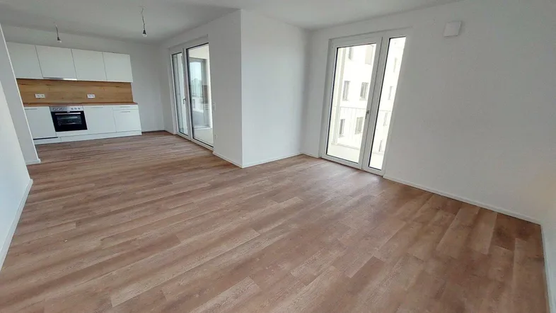 Heller offener Wohn-Essbereich mit integrierter Küche, modernem Boden und Zugang zum Balkon.