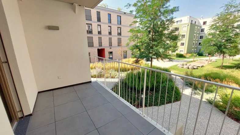 Heller Balkon mit modernen Fliesen und Blick auf die gepflegte Grünanlage und umliegende Gebäude.